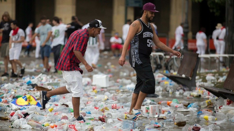 Dos jóvenes atraviesan el mar de basuras de la Plaza del Castillo en Sanfermines. EFE