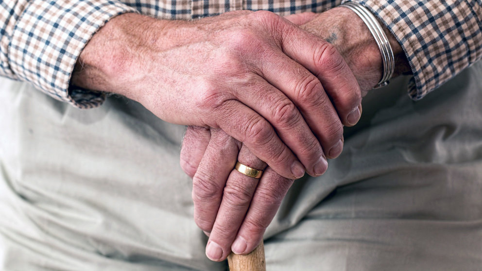 Un anciano sujeta un bastón entre sus manos.
