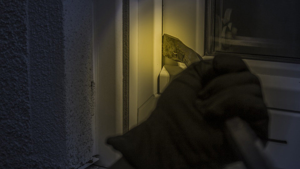 Un ladrón con guantes intentando abrir una puerta usando una palanca.