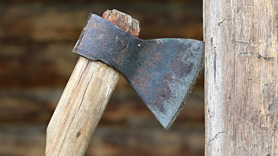 Imagen de un hacha, una herramienta empleada en muchas ocasiones como arma, clavada junto al tronco de un árbol ARCHIVO