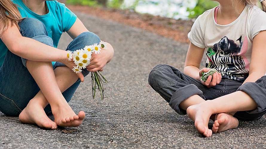 Dos niñas sentadas sobre el asfalto con unas flores en una imagen de recurso. ARCHIVO