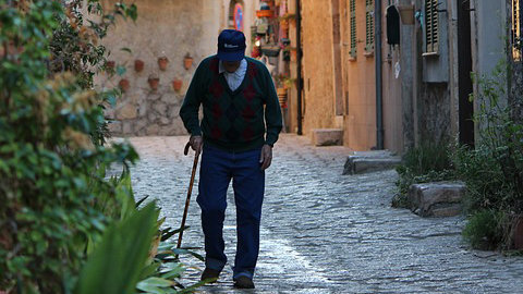 Un hombre de edad avanzada camina por la calle de un pueblo ayudándose con un bastón ARCHIVO