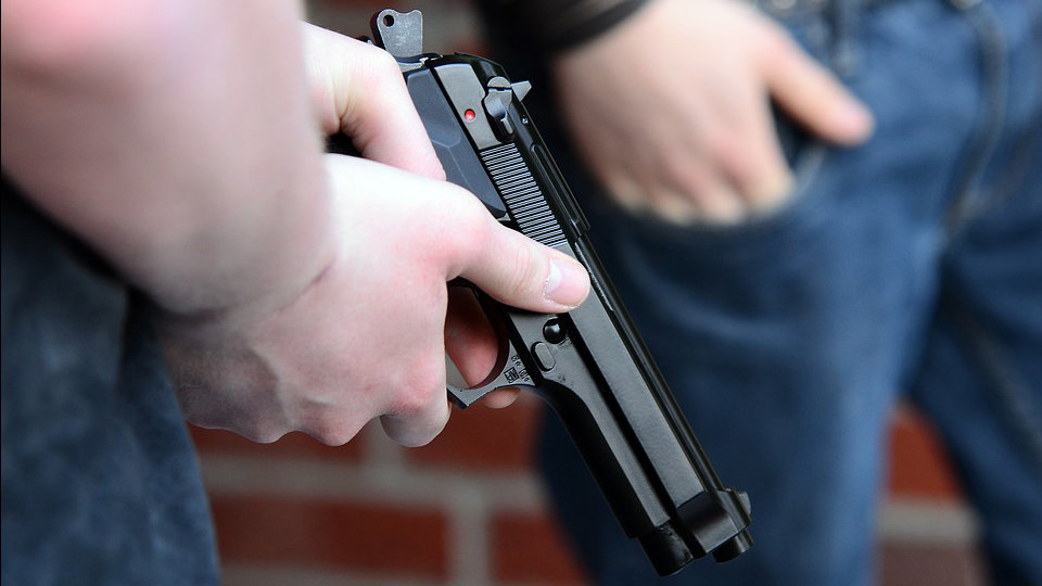 Un hombre empuñando una pistola en el barrio de una ciudad