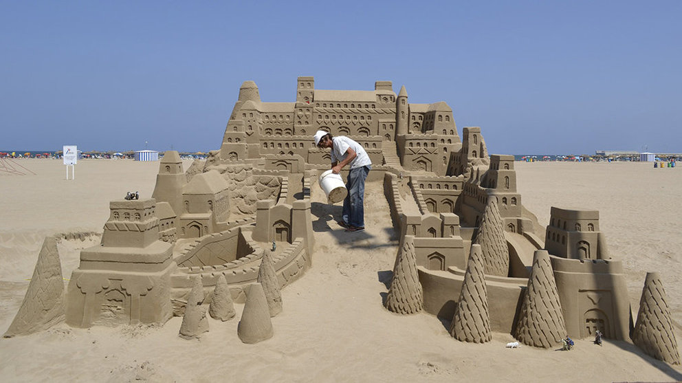Un hombre construye un castillo de arena en una playa. ARCHIVO