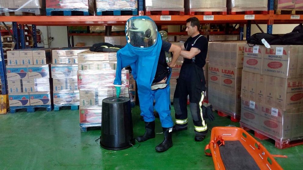 Un bombero se viste con el traje de protección química ayudado por un compañero en la fábrica de Cintruénigo