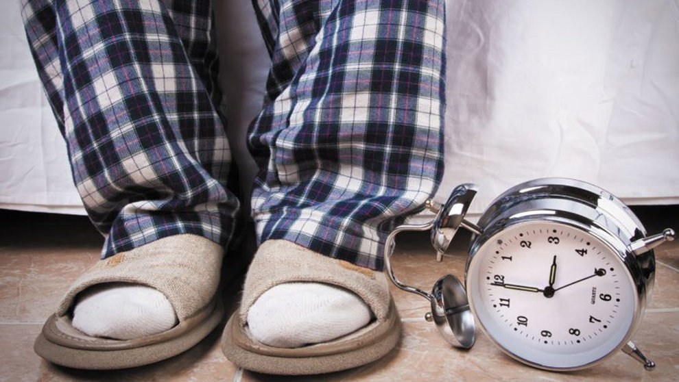 Un hombre en pijama y zapatillas de casa junto a un despertador ARCHIVO