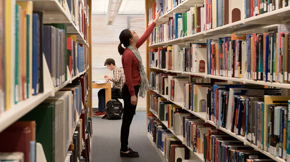 Una estudiante coge un libro de una estantería en una biblioteca. ARCHIVO