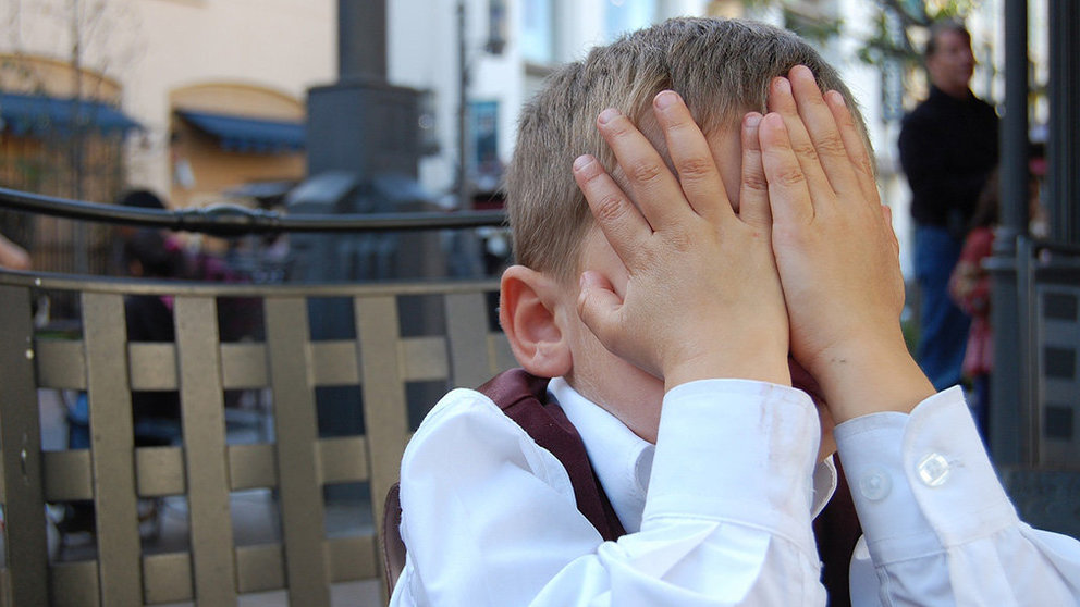 Un niño se tapa la cara con sus manos avergonzado.