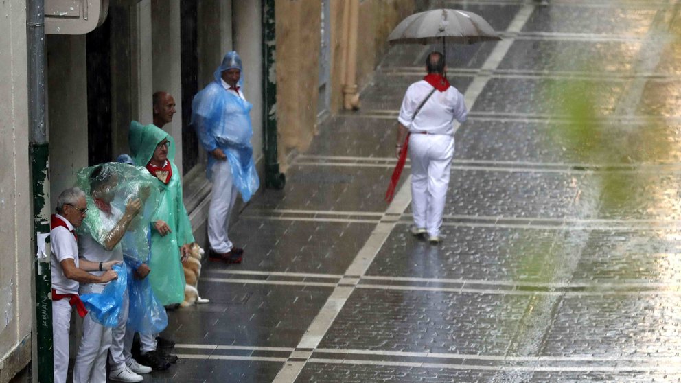 Dos personas se protegen de la lluvia en una de las céntricas calles de Pamplona, esta tarde durante la fiesta de San Fermín. Navarra está en alerta amarilla este lunes por lluvias y tormentas, según datos de la web de la Agencia de Meteorología (Aemet). EFE/ Javier Lizón