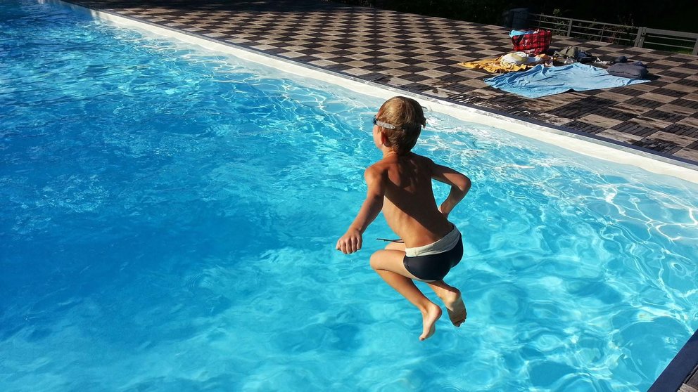 Un niño salta a una piscina desde el bordillo
