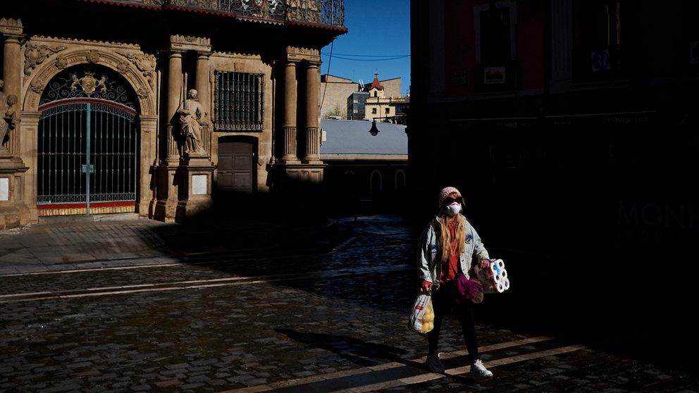 Una mujer con una mascarilla y cargada con artículos de supermercado camina por la Plaza del Ayuntamiento de Pamplona. PABLO LASAOSA