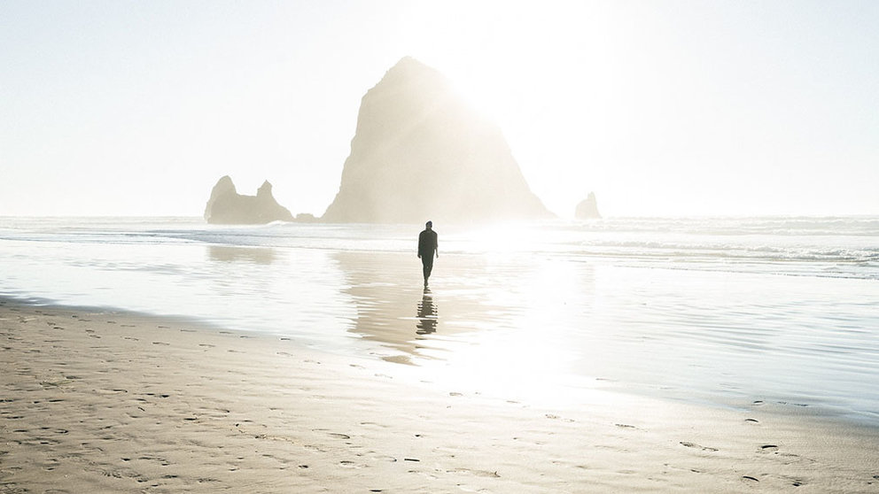 Un hombre pasea por una playa vacía durante un atardecer.