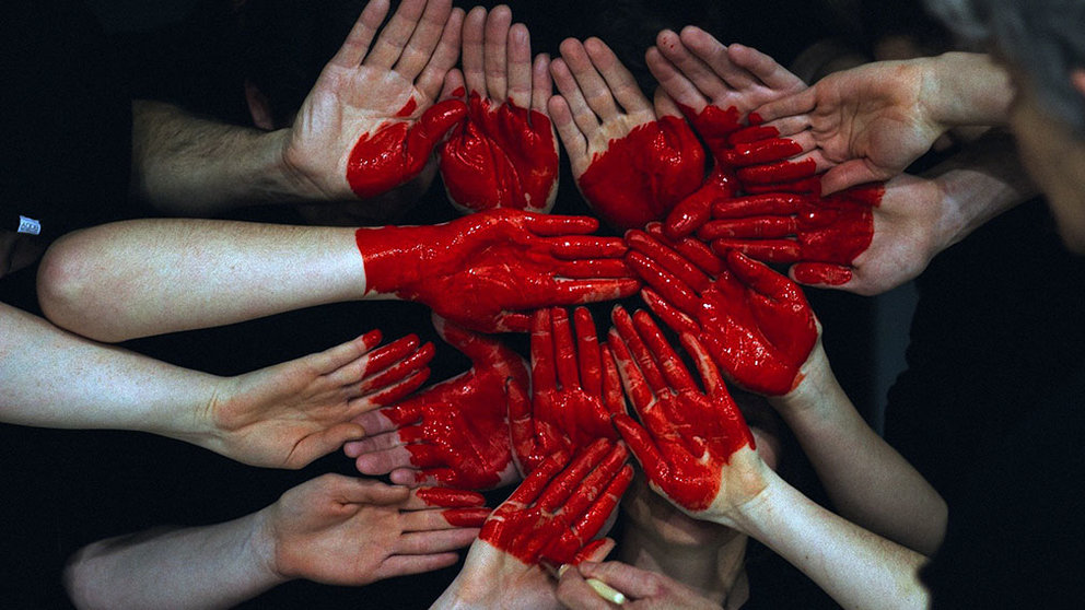 Una pintora dibuja con color rojo sobre las manos de otras personas. 