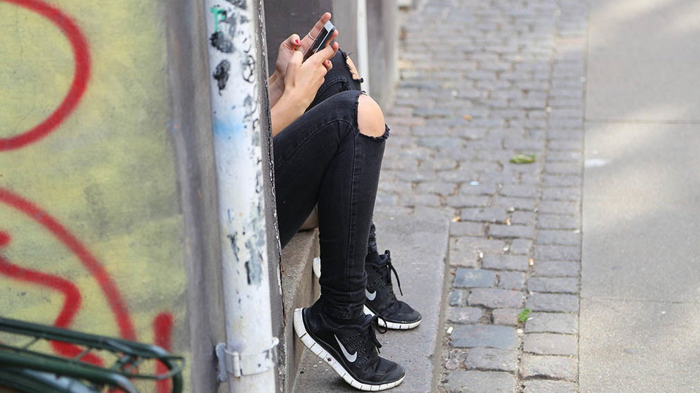 Una chica consulta su teléfono móvil sentada en un portal de la calle. ARCHIVO.