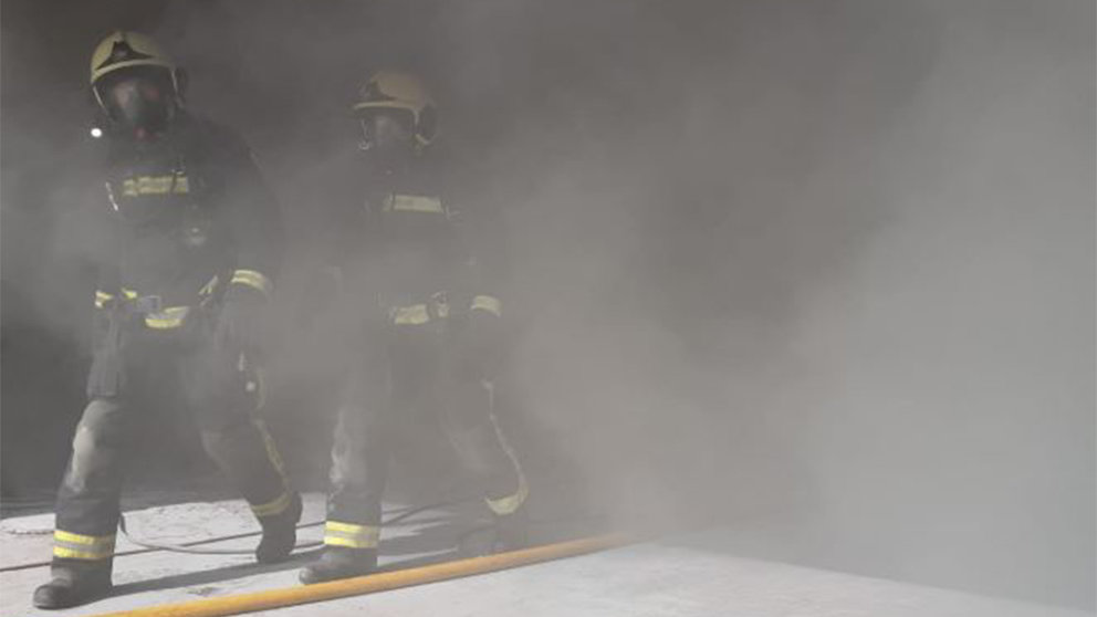 Dos bomberos salen del interior de la empresa, ubicada en el polígono Talluntxe, donde hubo un incendio. BOMBEROS DE NAVARRA