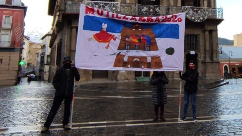 Tres representantes de la peña Mutilzarra extienden la pancarta sanferminera de 2020 para despedir el año. CEDIDA