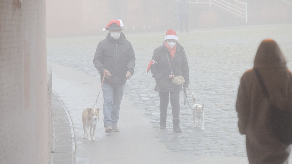 Dos personas ataviadas con gorros navideños cruzan la Plaza de los Fueros paseando a sus perros.
Pamplona encadena dos semanas seguidas amaneciendo bajo una densa niebla. IÑIGO ALZUGARAY