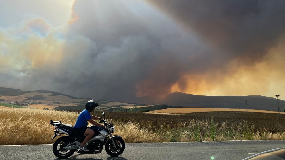 Una persona circula en moto este sábado en la localidad de Astráin (Pamplona) desde donde se puede apreciar un incendio. EFE / Villar López