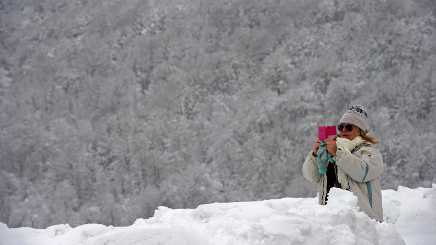 Una mujer realiza una fotografía en el Alto de Ibañeta (Navarra) que hoy ha amanecido nevado debido a la progresiva bajada de la cota de nieve, y que ha hecho que durante la noche se movilicen máquinas quitanieves de forma preventiva. EFE/VILLAR LÓPEZ