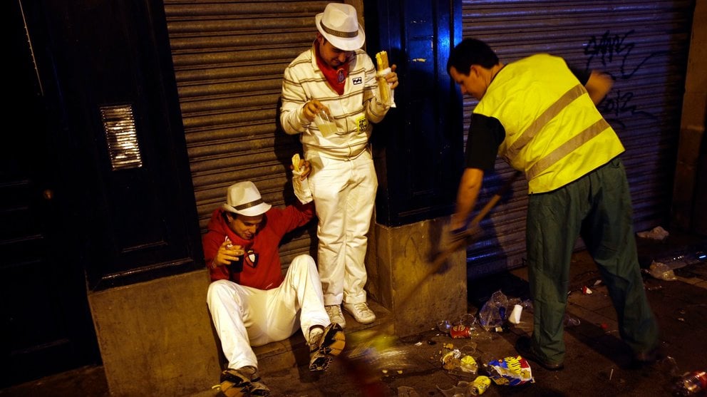 Revellers react as a municipal worker sweeps garbage from under their feet while they wait for the start of the fifth running of the bulls at the Estafeta corner during San Fermin festival in Pamplona July 11, 2012. Several runners suffered light injuries in a run that lasted three minutes and twelve seconds, according to local media. REUTERS/Susana Vera (SPAIN - Tags: SOCIETY TPX IMAGES OF THE DAY) SPAIN/