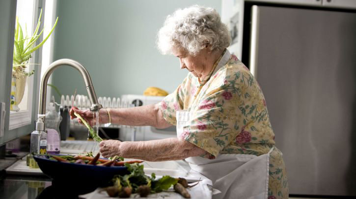 Imagen de archivo de una mujer de edad avanzada limpiando verdura en la cocina de su casa