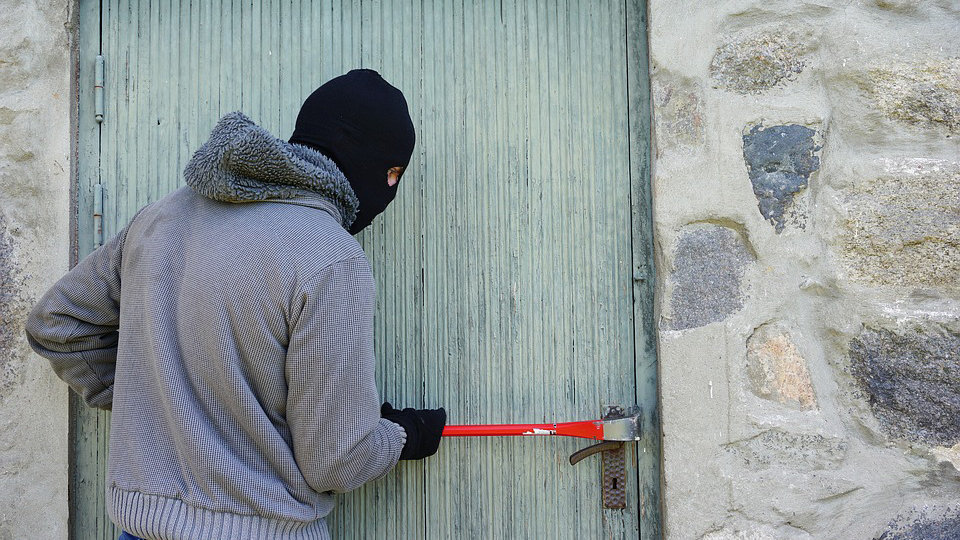 Imagen de un ladrón encauchado forzando una cerradura de una vivienda para entrar a robar ARCHIVO