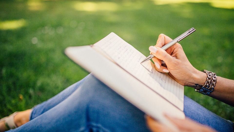Una chica escribe un relato en un cuaderno mientras disfruta del buen tiempo en un parque ARCHIVO