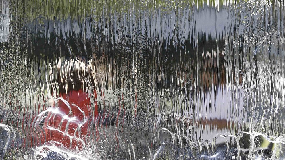 Una cortina de agua difumina la figura de dos personas que disfrutan de una tarde soleada en un parque de Pamplona en una jornada donde el calor ha sido el protagonista en toda Navarra. EFE/Jesús Diges