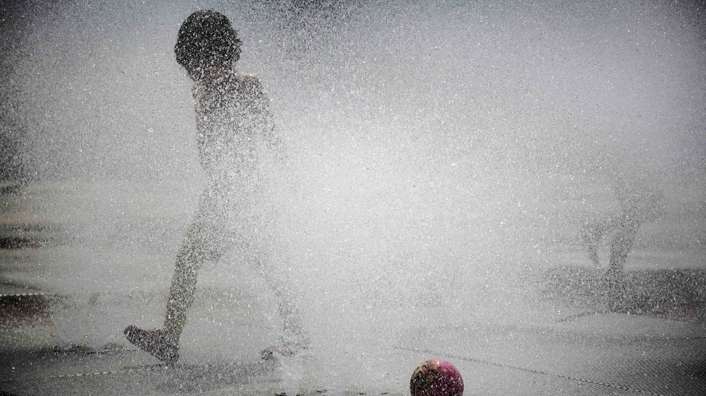 Un niño se divierte con el agua de una fuente de Pamplona, en una jornada donde las temperaturas han alcanzado los 33 grados en la capital navarra y el cielo aparece completamente despejado. EFE/Villar López