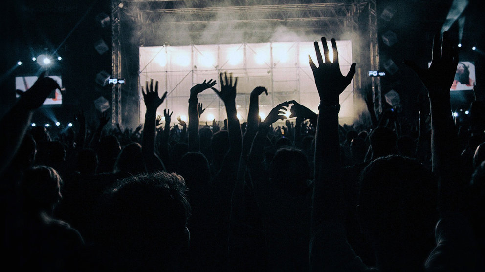 Varios jóvenes bailan en una discoteca con sus brazos en alto.