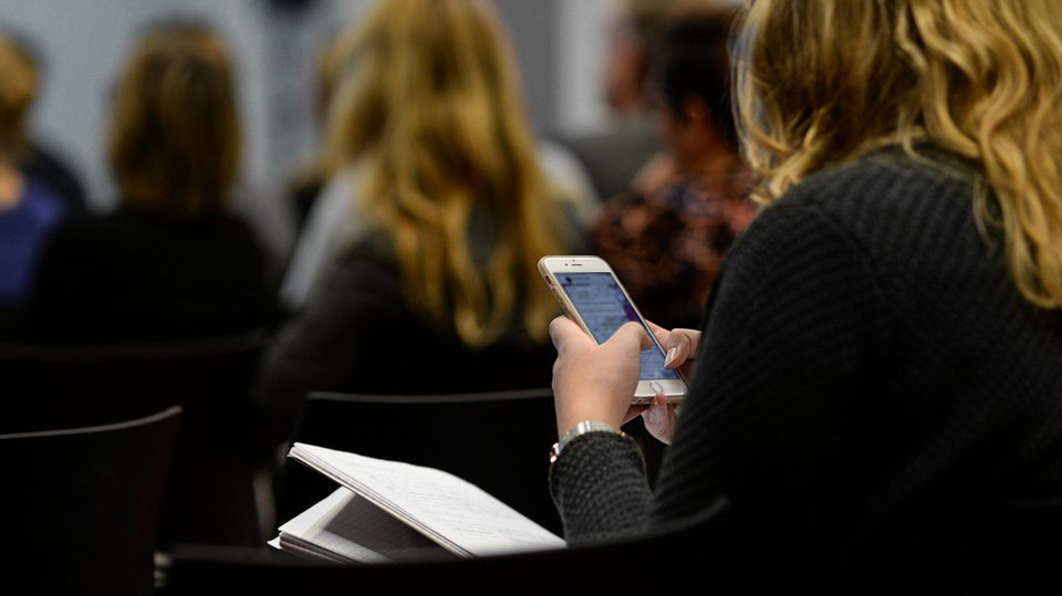 Una mujer escribe un mensaje a través de su teléfono móvil en una reunión ARCHIVO
