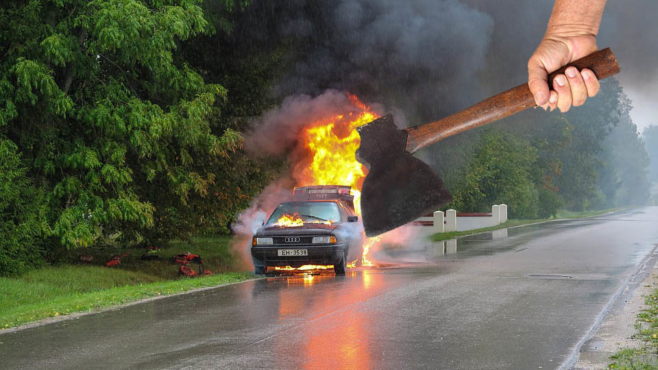 Un hombre sostiene un hacha delnate de un coche ardiendo FOTOMONTAJE
