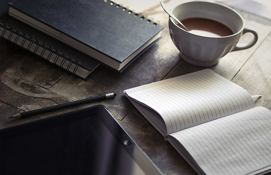 Una persona trabaja junto a su bloc de notas y su iPad junto a un café..