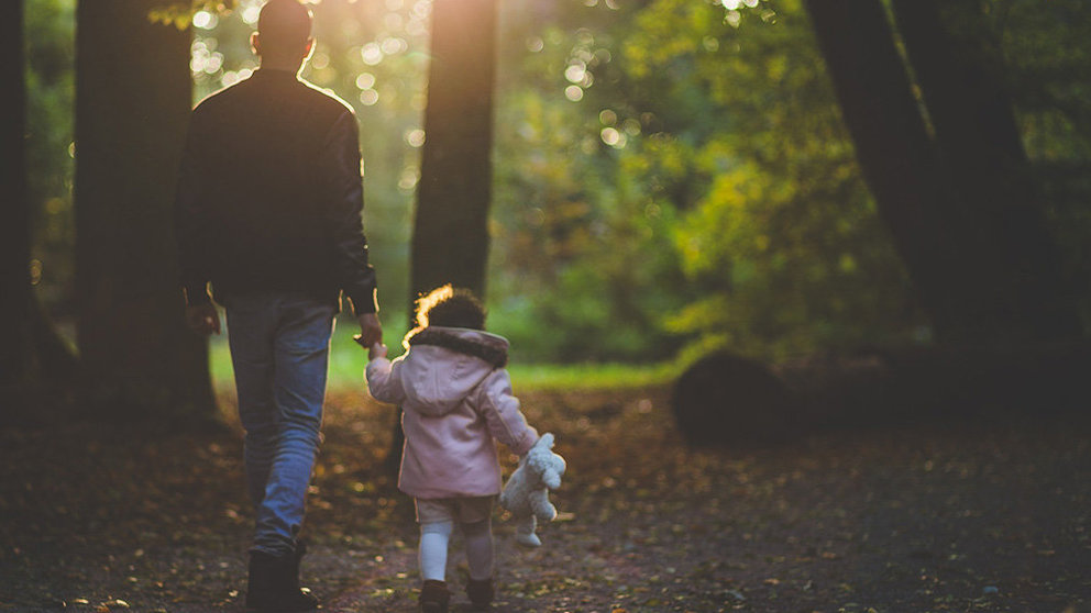 Un padre pasea con su hija por el camino de un bosque