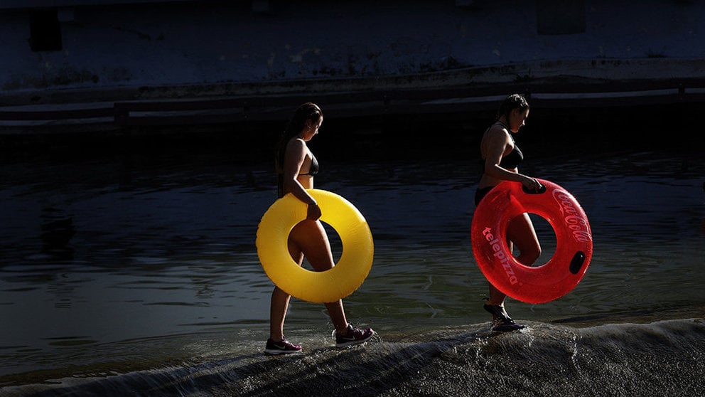 Varios jóvenes con unos flotadores se divierten en el río Arga a su paso por Pamplona en un día marcado por el tiempo soleado y el calor veraniego. EFE/Villar López