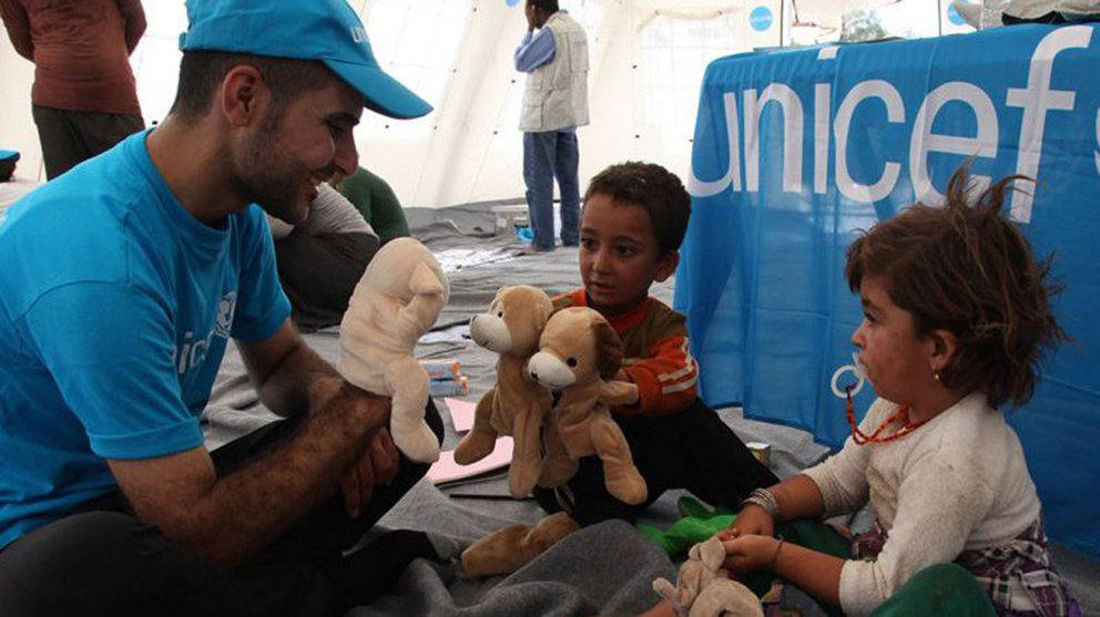 Un voluntario de UNICEF anima a unos niños jugando con ellos en un campamento gestionado por la organización solidaria UNICEF