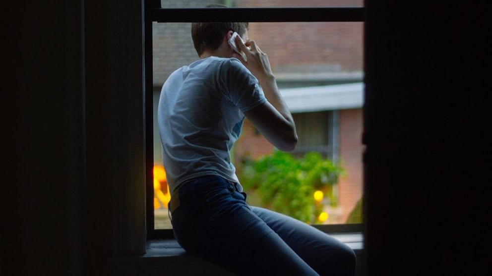 Un joven habla por teléfono asomado a una ventana. ARCHIVO
