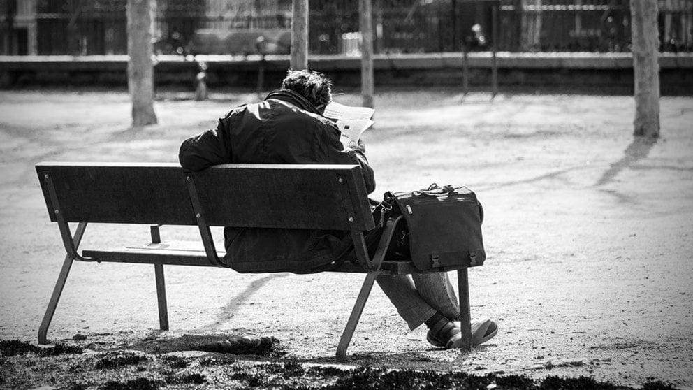 Un hombre lee sentado en un banco de la calle.