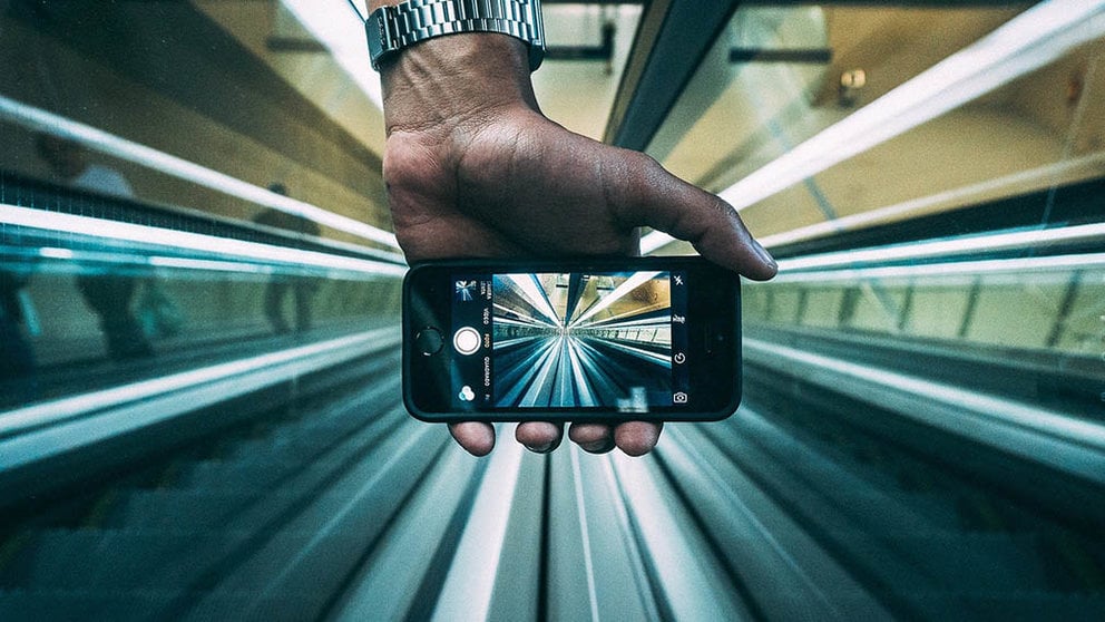 Un hombre toma una fotografía en una escaleras mecánicas.