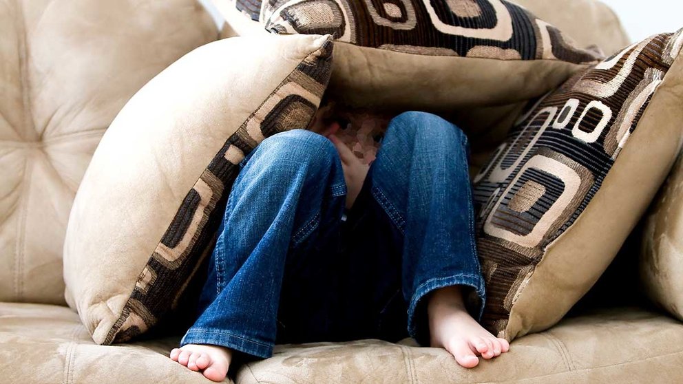 Una niña se esconde atemorizada entre los cojines de un sofá. ARCHIVO