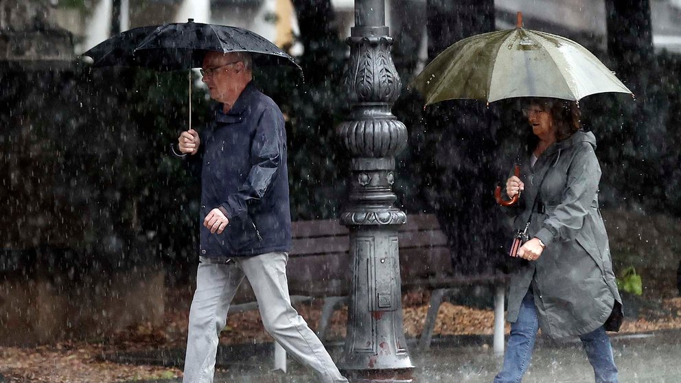 Dos personas se protegen de la lluvia con sus paraguas en una jornada donde el ambiente inestable, con chubascos localmente fuertes y de cierta intensidad continúa en la Comunidad Foral.  EFE/ Jesús Diges